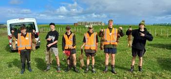 A group of people in orange vests standing in a field

Description automatically generated