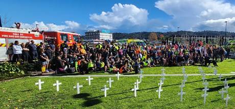 A group of people sitting on grass with white crosses

Description automatically generated