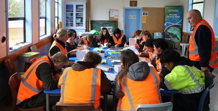 A group of people in orange vests sitting at a table

Description automatically generated
