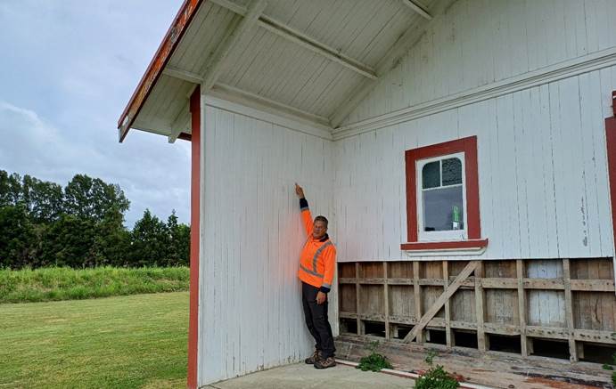 A person in an orange vest standing in front of a white house

Description automatically generated